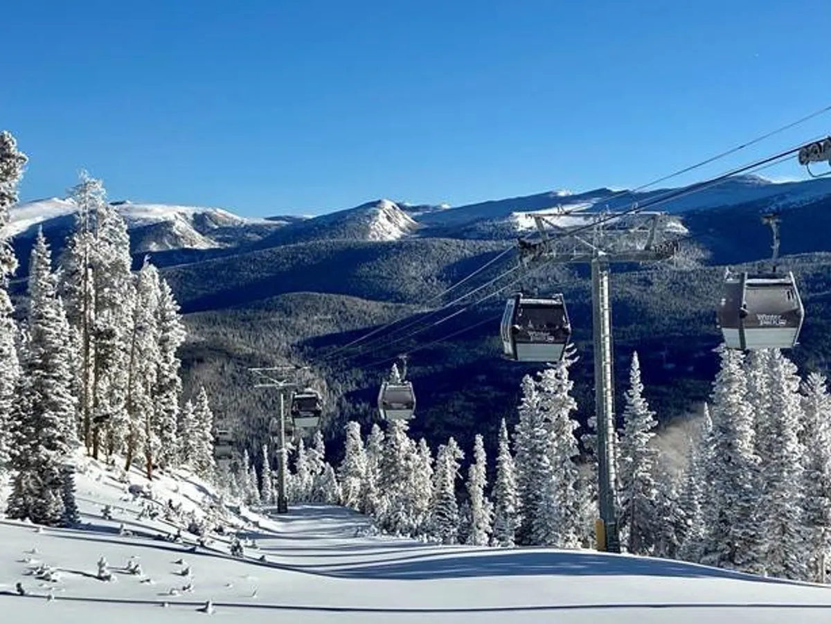 A stunning exterior view of gondola lifts gliding over snow-covered trees and a majestic mountain range, beneath a crisp blue sky. The landscape evokes the sense of outdoor exploration, scenic beauty, and adventure that makes the area such a great getaway for dog owners.