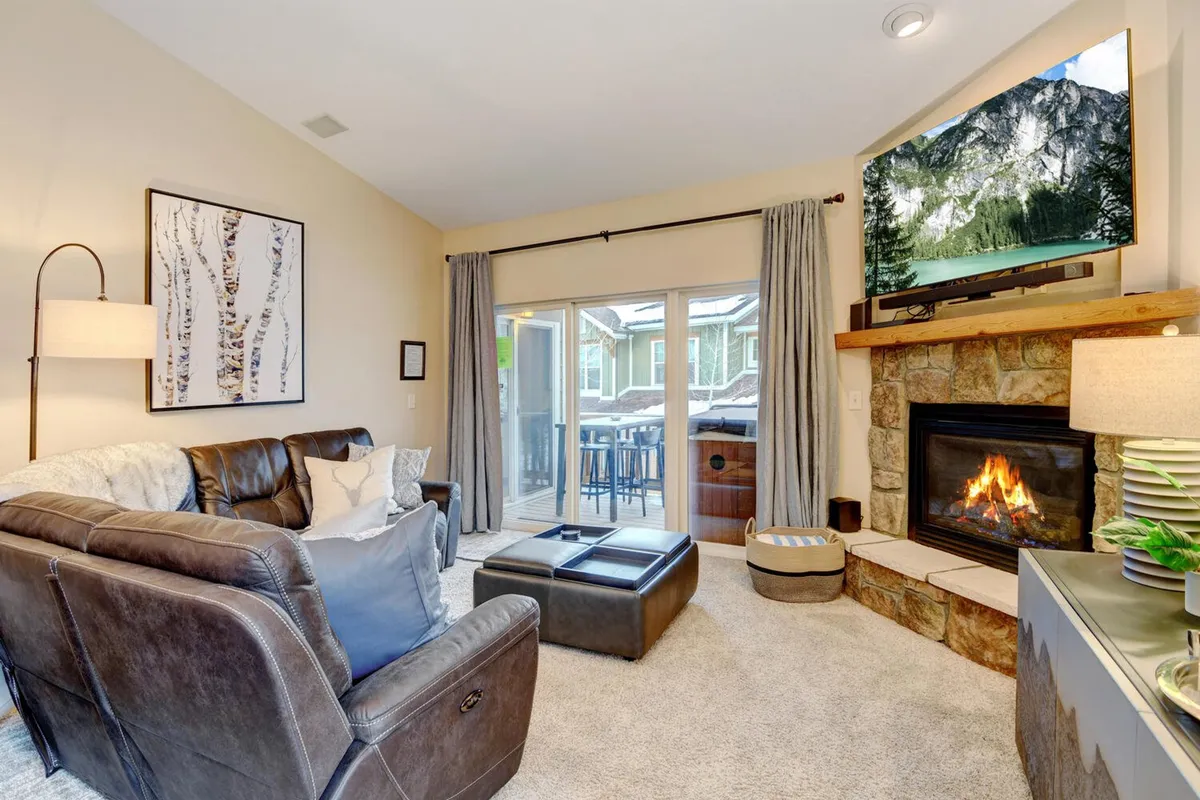 A cozy living room featuring a comfortable sofa arranged before a fireplace and a wall-mounted TV. Large sliding glass doors flood the room with natural light and offer a view and access to the outdoor patio or balcony area. The inviting layout encourages relaxation, movie nights, and social gatherings.