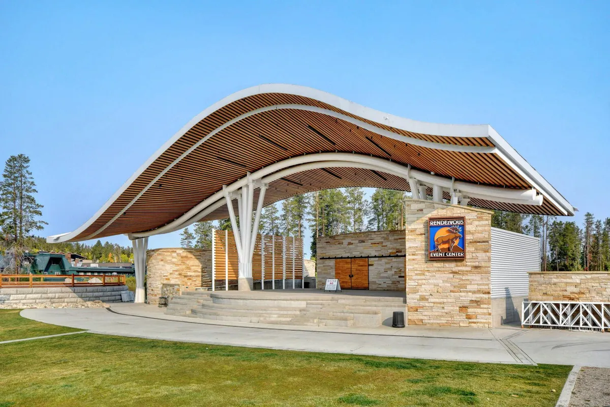 An exterior shot featuring the curved roof structure and stone wall of the Hideaway Park amphitheater, with event signage visible. The area is set up to host community events, concerts, and gatherings, giving a sense of the lively local entertainment scene just steps from the villa.