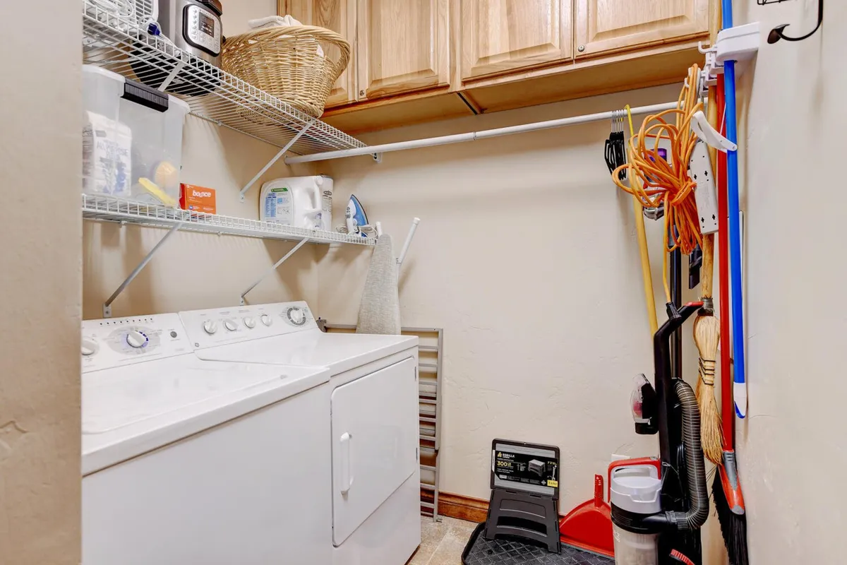 A dedicated laundry area with a washing machine, dryer, neatly arranged shelves, and cleaning tools. The space feels organized and practical for guests' convenience.