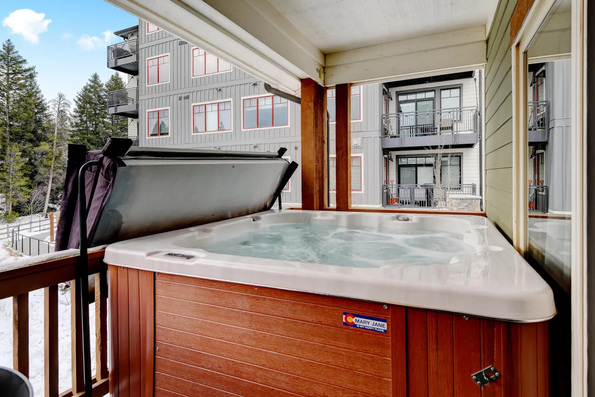 An outdoor hot tub on a private balcony, surrounded by trees and shielded by a railing. The serene setting invites guests to soak while enjoying tranquil mountain views, fresh air, and the peaceful ambiance of the outdoors.